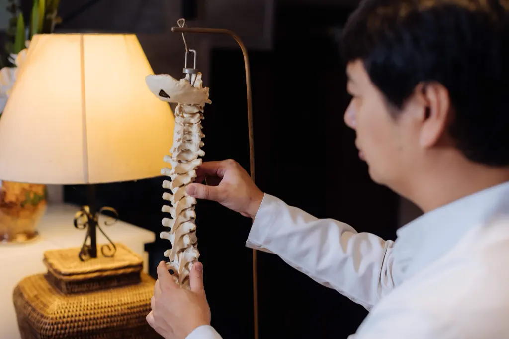 Dr. Marcus Yu Bin Pai examina um modelo de coluna vertebral no consultório.