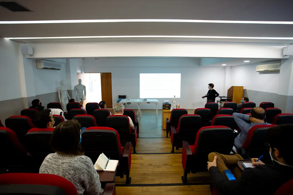 Auditório com poltronas vermelhas e plateia diante de uma apresentação.