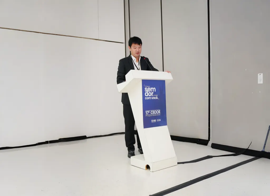 Dr. Marcus Yu Bin Pai em pé ao púlpito do 17º CBDOR, em uma sala branca.